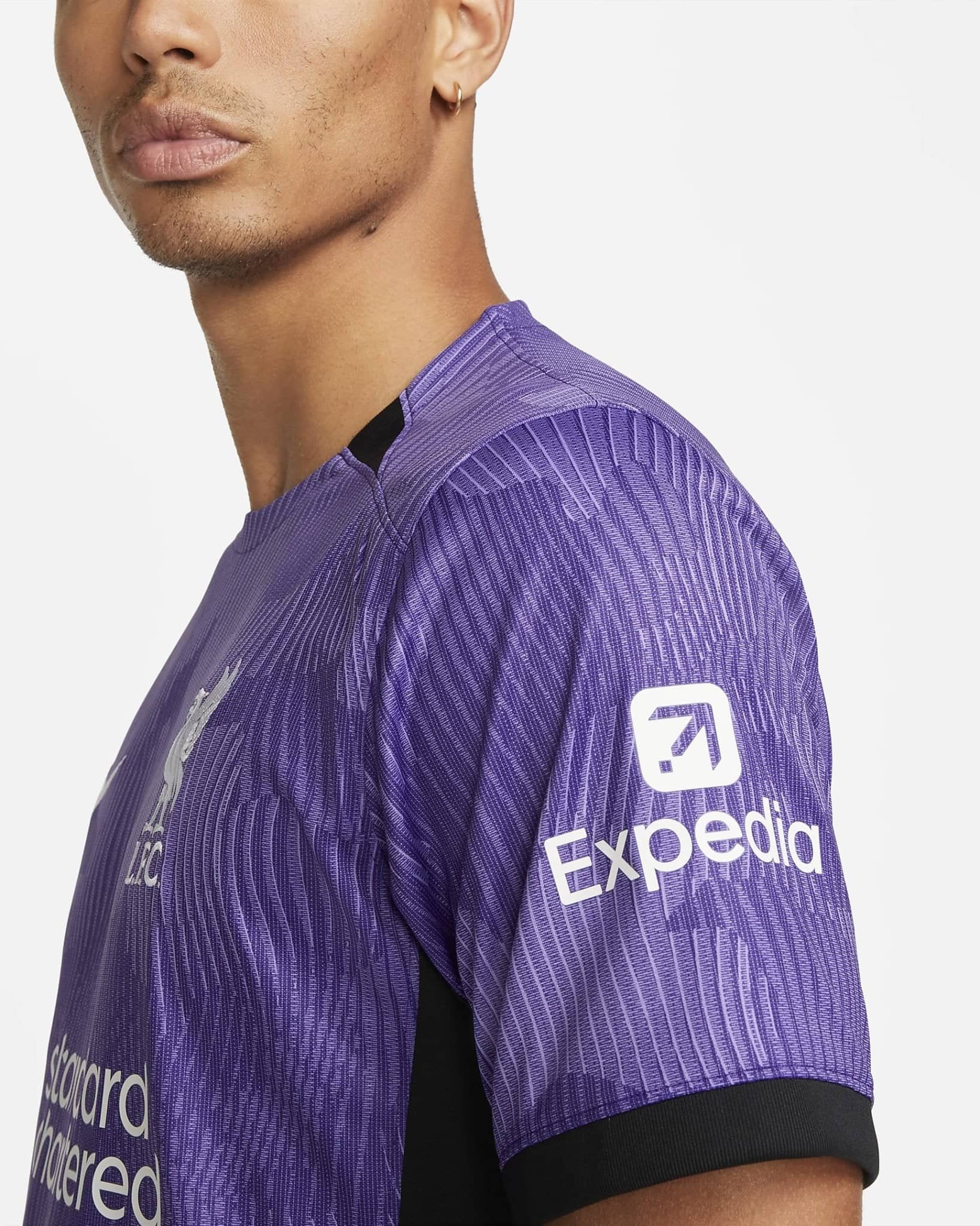 liverpool-third-jersey-202324-113436_1 | AE JERSEY Close-up of a person’s shoulder and neck wearing a purple striped athletic jersey, with a white logo on the sleeve.