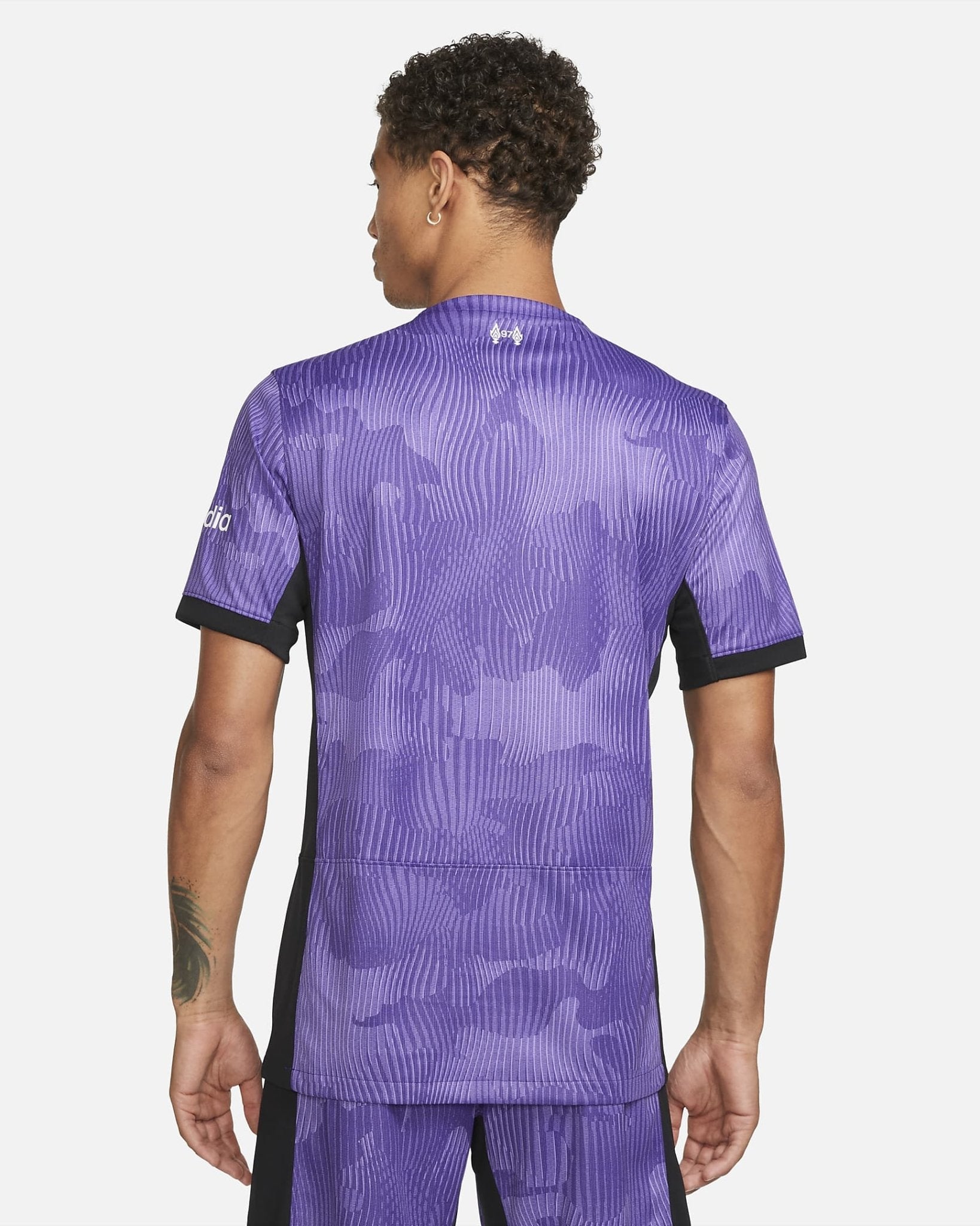 liverpool-third-jersey-202324-339931_b332c077-a55f-4568-865a-6984bc45b2f9 | AE JERSEY Back view of a person wearing a purple camo-pattern athletic jersey with black side panels, short sleeves, and a small logo at the neck.