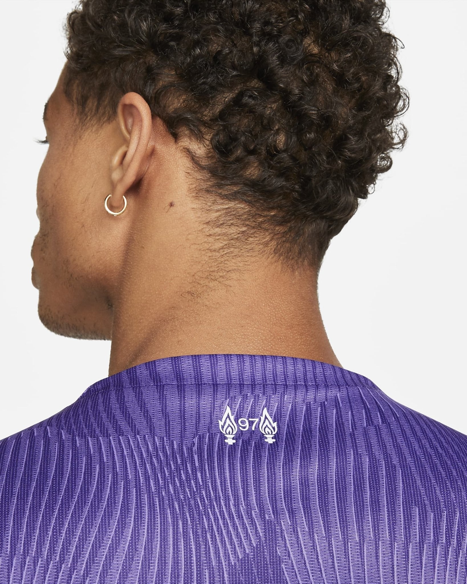 liverpool-third-jersey-202324-566581_3de9d7ff-9a16-498b-941b-aef0420cd336 | AE JERSEY Back view of a person with short, curly hair and a small gold hoop earring, wearing a purple striped shirt with the number 97 and flame icons on the back.