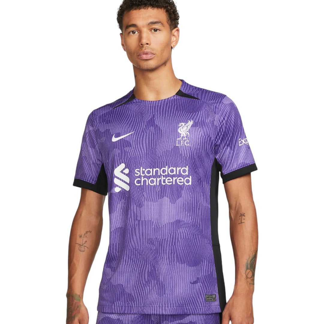 liverpool-third-jersey-202324-772831_844932b5-4101-445e-8e01-a61f549f2655 | AE JERSEY Young man wearing a purple Liverpool FC jersey with Standard Chartered sponsor logo front and crest on chest.