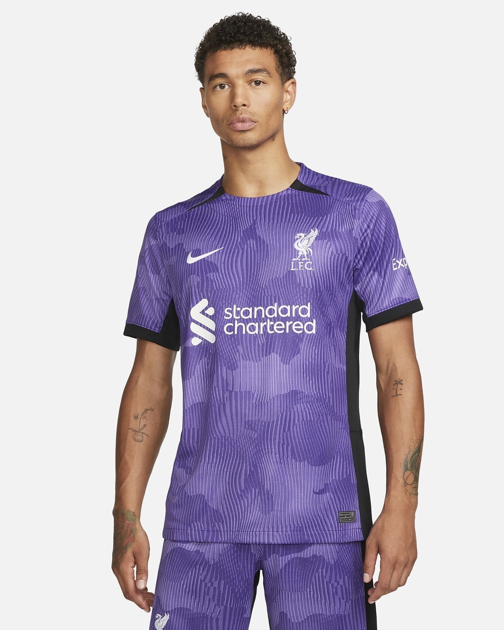 liverpool-third-jersey-202324-930859_d8493d2d-c791-41d3-8502-e47b192f4af4 | AE JERSEY Man modeling a purple Liverpool FC football jersey with Standard Chartered logo, front view against a light background.
