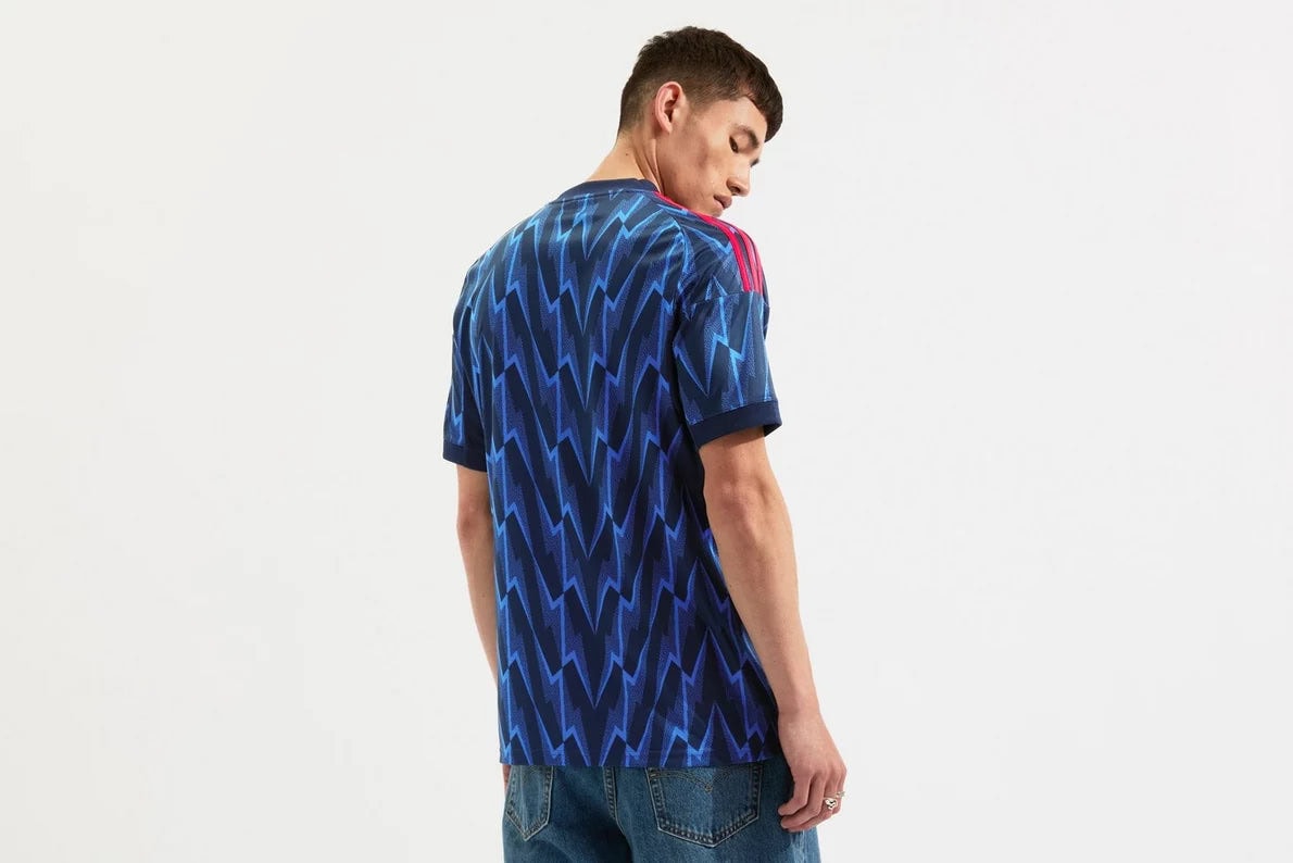 mji9511_b | AE JERSEY Man wearing a blue zigzag-patterned short-sleeve shirt shown from the back, with red accents on the shoulders, paired with jeans.