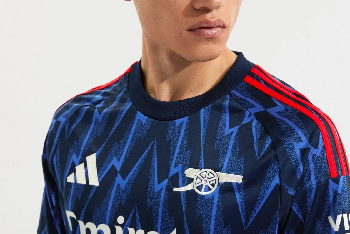mji9511_d | AE JERSEY Man wearing a navy blue zigzag-pattern soccer jersey with red shoulder stripes and white logos.