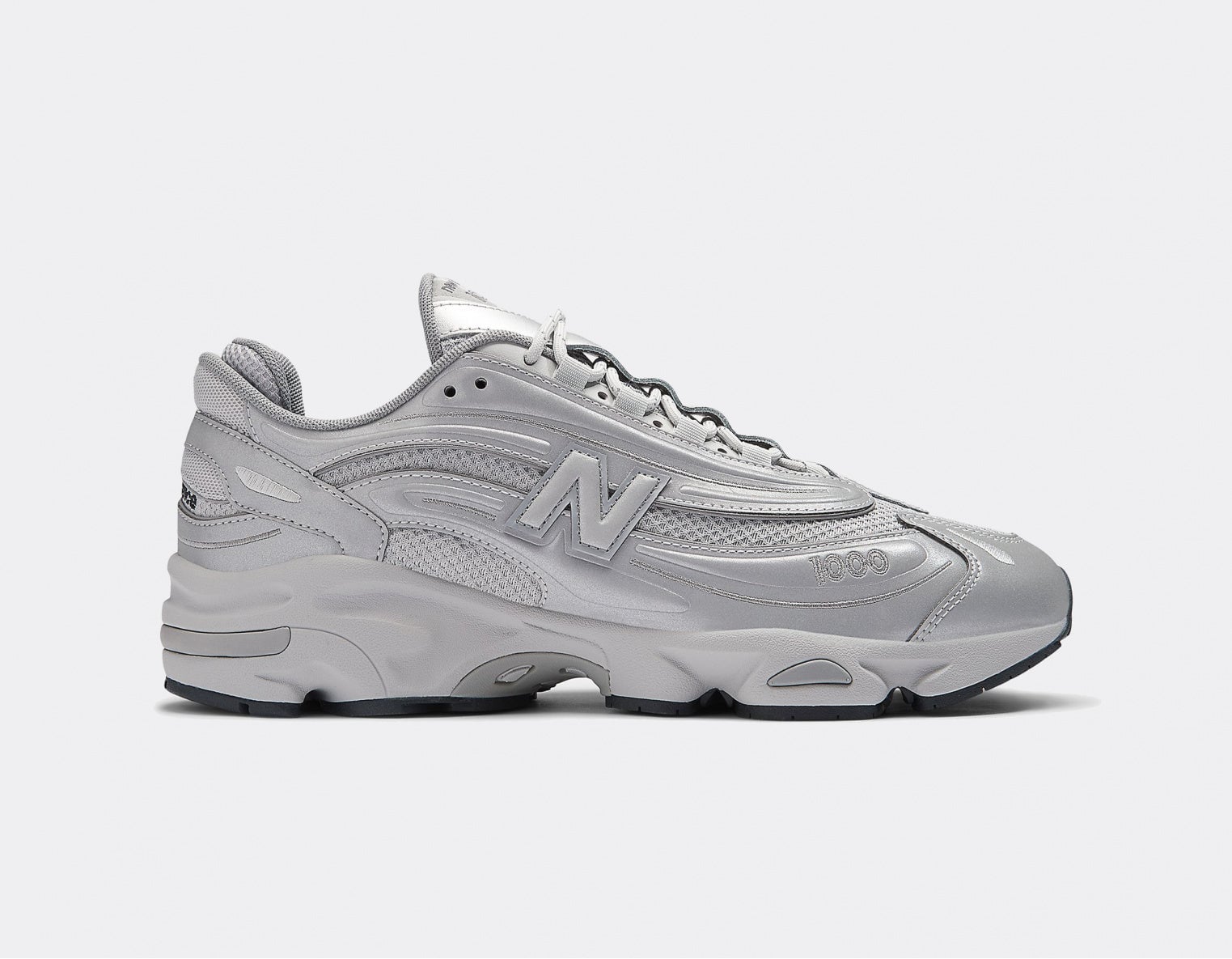 new-balance-m1000-te-reflective-pack-silver | AE JERSEY Side view of a bulky gray athletic sneaker with a thick sole and stitched panels, featuring an NB 'N' logo and '1000' on the toe area