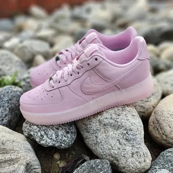 nike-nocta-air-force-1-low-pink-girls-for-women-bsf372-1-600x600-1 | AE JERSEY Light pink Nike sneakers resting on gray rocks outdoors, showing laces and side swoosh detail