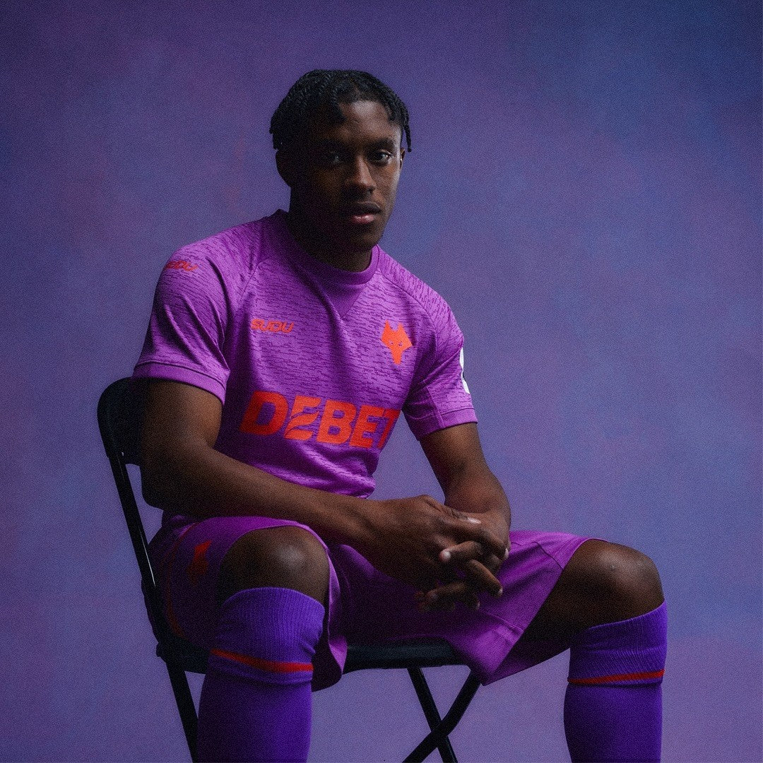 obOQeh7eS2Zoffk | AE JERSEY Athlete in a purple soccer kit sits on a folding chair, gazing at the camera against a purple studio backdrop.