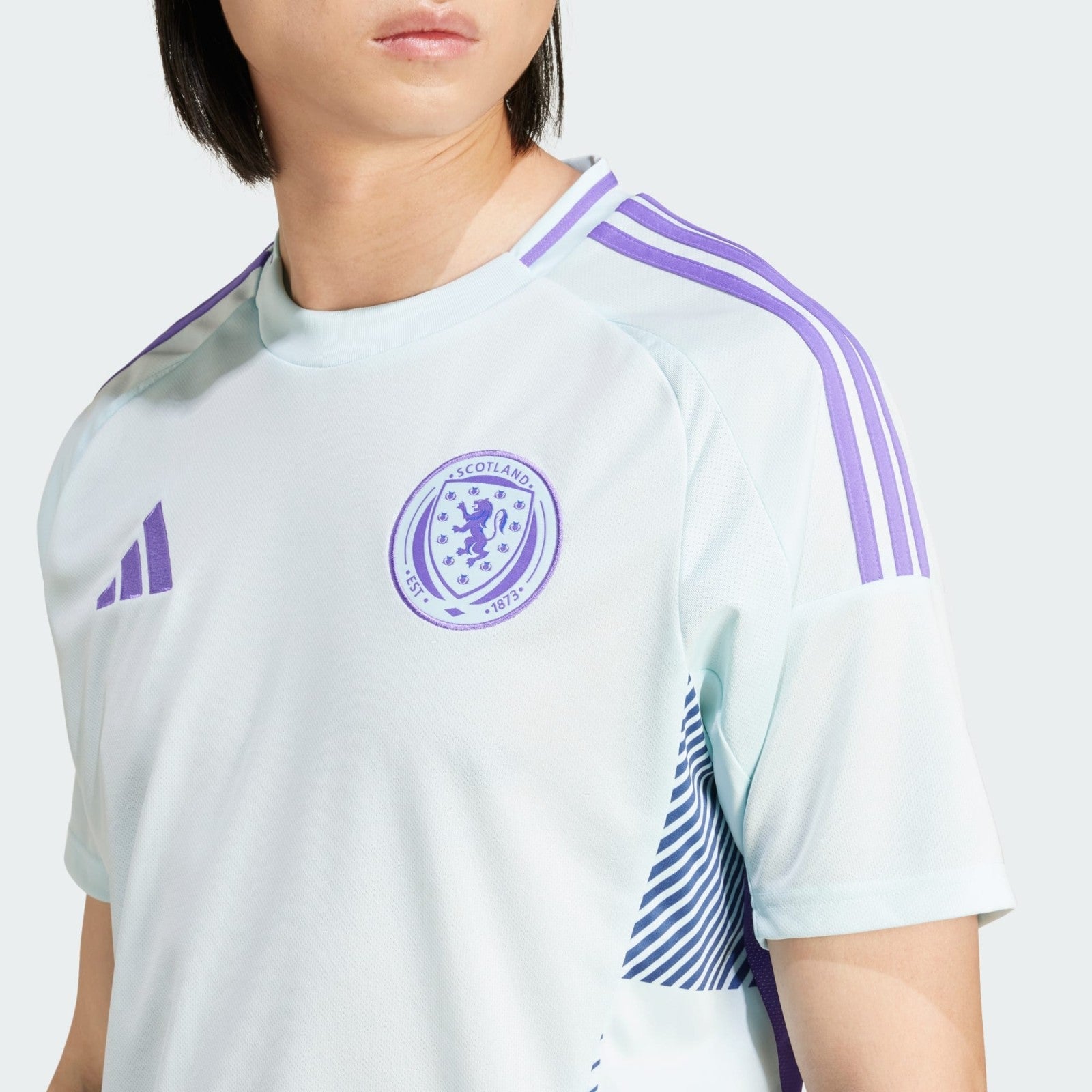 rKsBjstQIEkH4co | AE JERSEY Close-up of a person wearing a light blue Scotland football jersey with purple Adidas stripes on the shoulder and the crest on the chest.