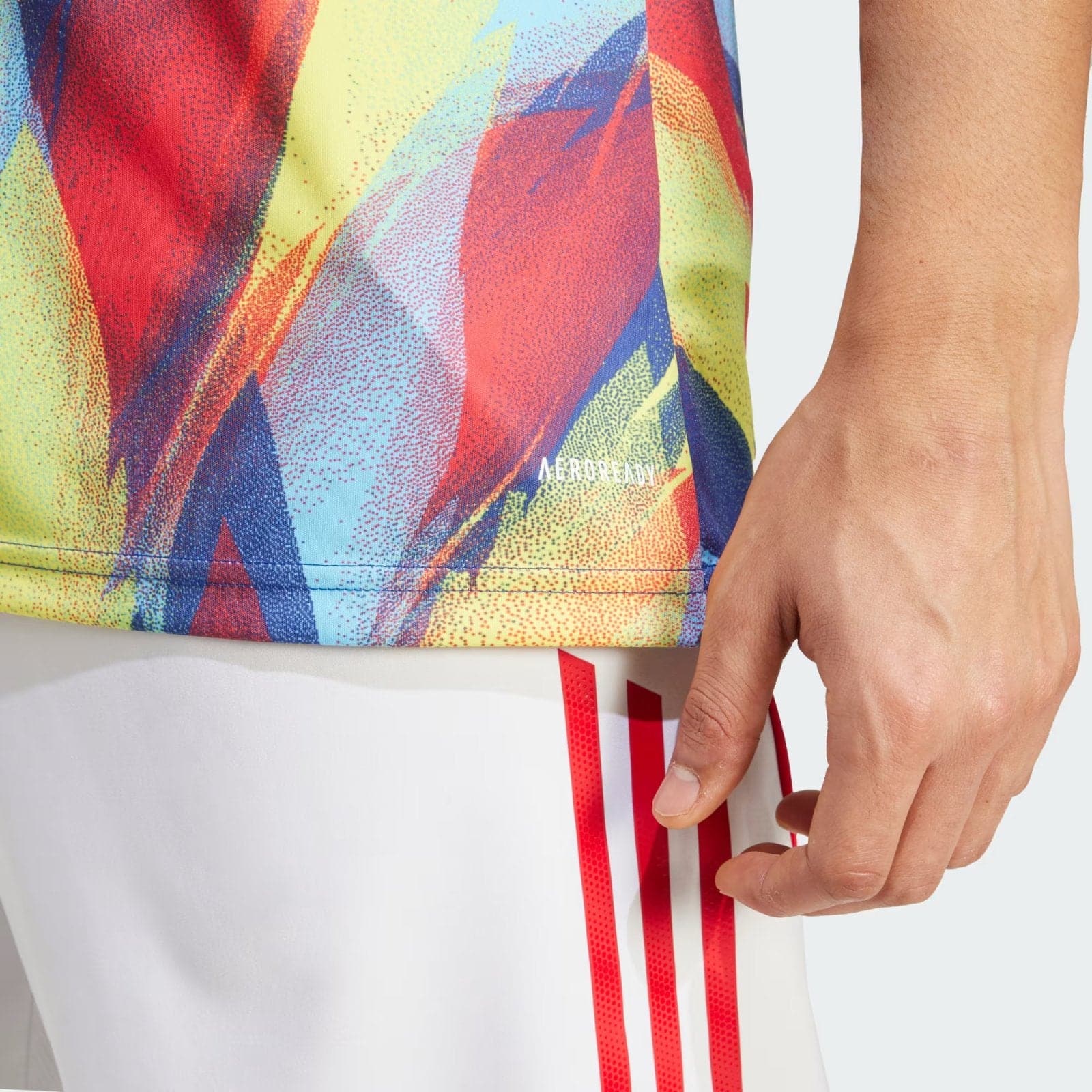 rZJsNA3lhwlIpEN | AE JERSEY Close-up of a colorful abstract sports fabric with a hand resting nearby and a small 'AEROREADY' logo visible on the material.