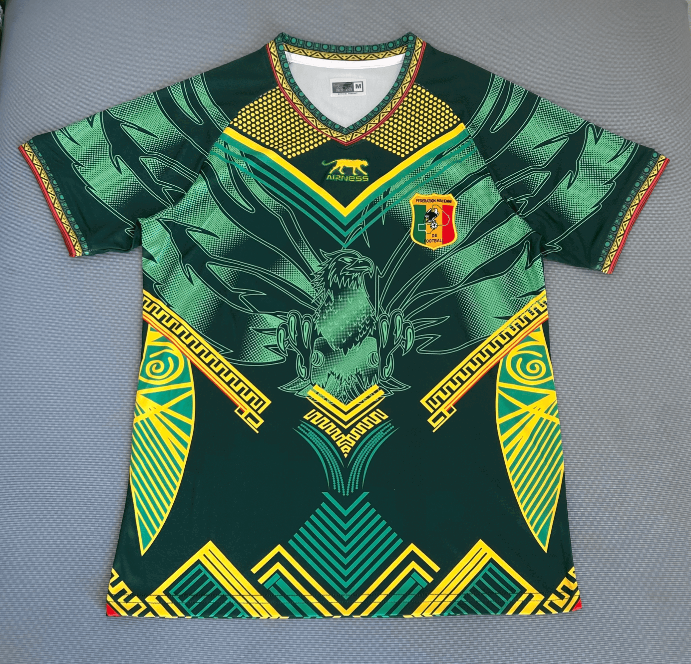 rn-image_picker_lib_temp_01efba58-5db6-4fbc-b9b8-dc21dc6d672d | AE JERSEY Green football jersey with yellow and teal geometric patterns and a shield crest reading Federation Malienne de Football on the chest, featuring an eagle motif.