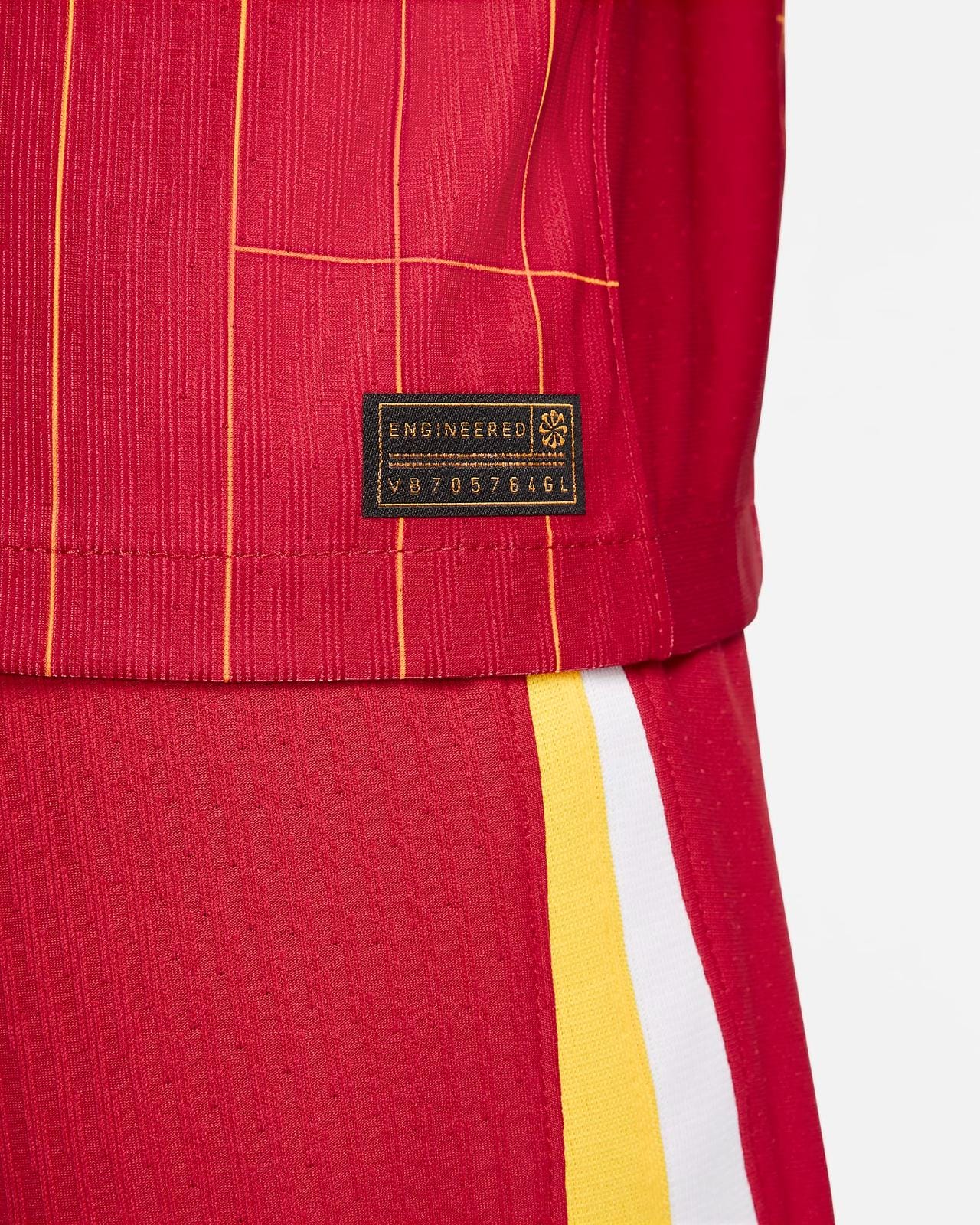rn-image_picker_lib_temp_1ed96907-a024-4e32-9153-9d827db5b9df | AE JERSEY Close-up of red fabric with yellow piping and a black tag reading ENGINEERED near the hem.