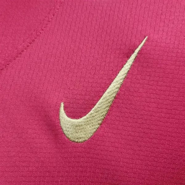 rn-image_picker_lib_temp_37655ca5-fa5b-4155-a52a-3258d4007f2f | AE JERSEY Gold Nike swoosh embroidered on bright pink fabric.