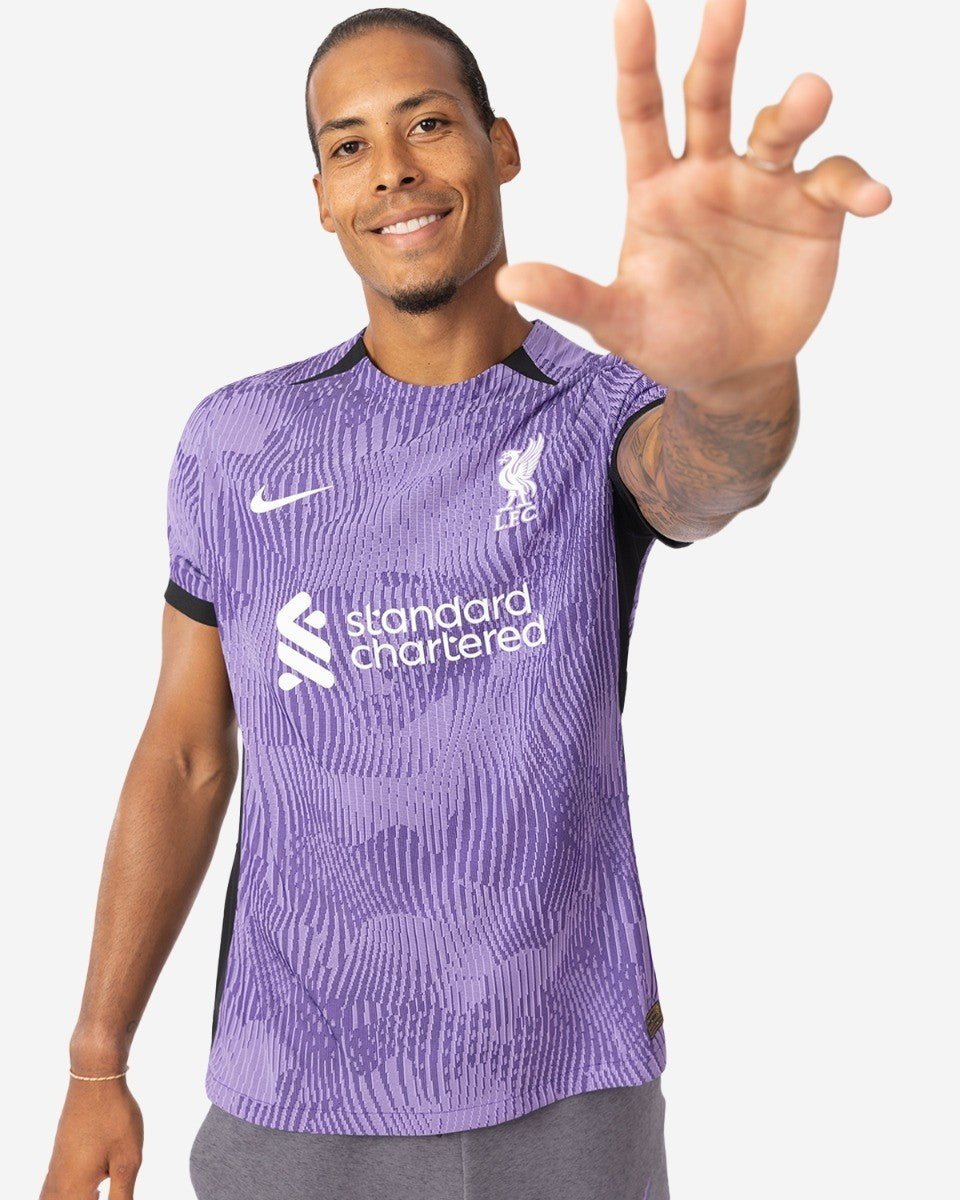 rn-image_picker_lib_temp_5984ad00-a5bf-47f1-a8e2-95ec784e5f3d | AE JERSEY Man in a purple Liverpool FC jersey smiles and reaches his hand toward the camera.