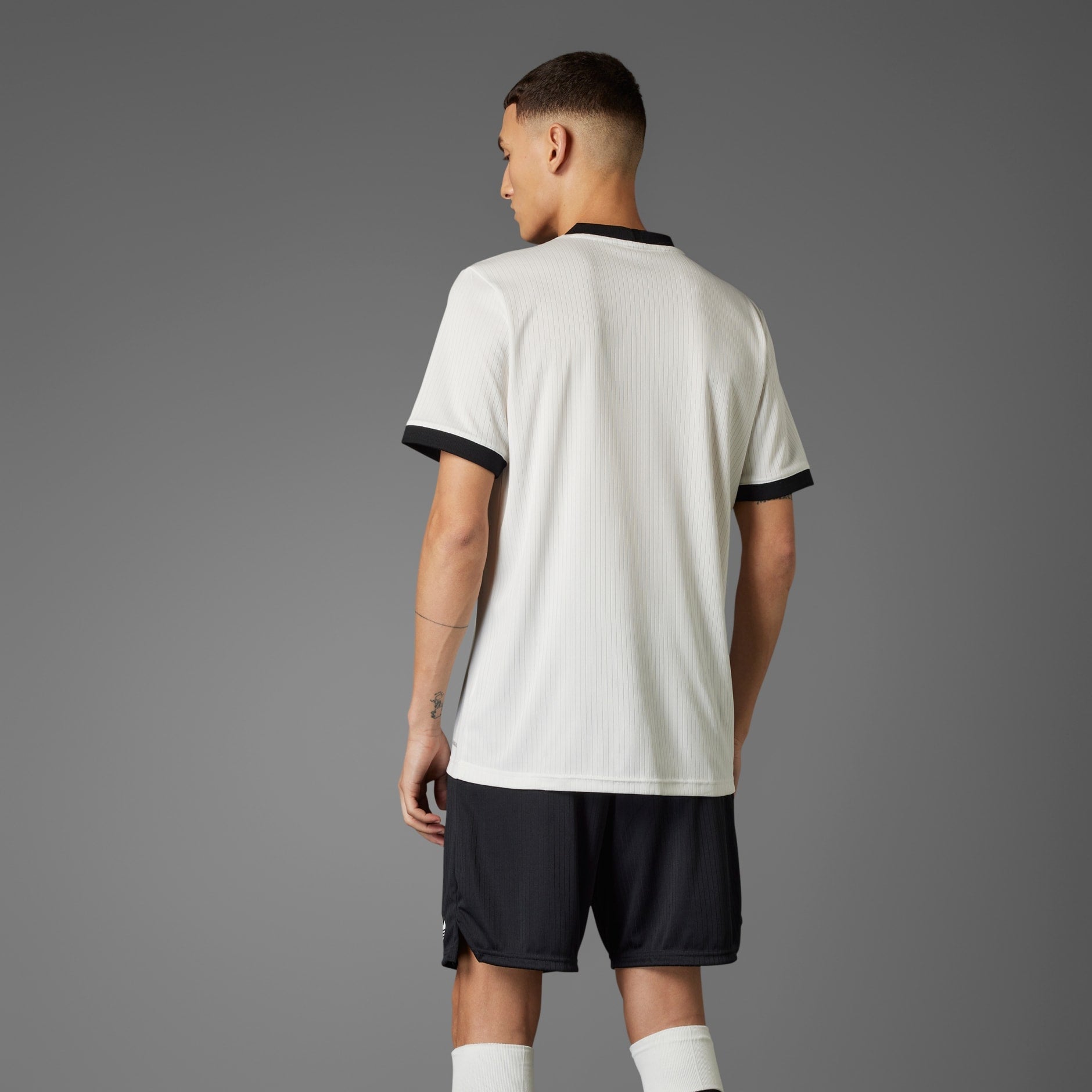 rn-image_picker_lib_temp_5c745790-c83b-4b8f-bf3c-736f49f09d1a | AE JERSEY Back view of a person wearing a white sports jersey with black cuffs against a gray background, seen from behind.