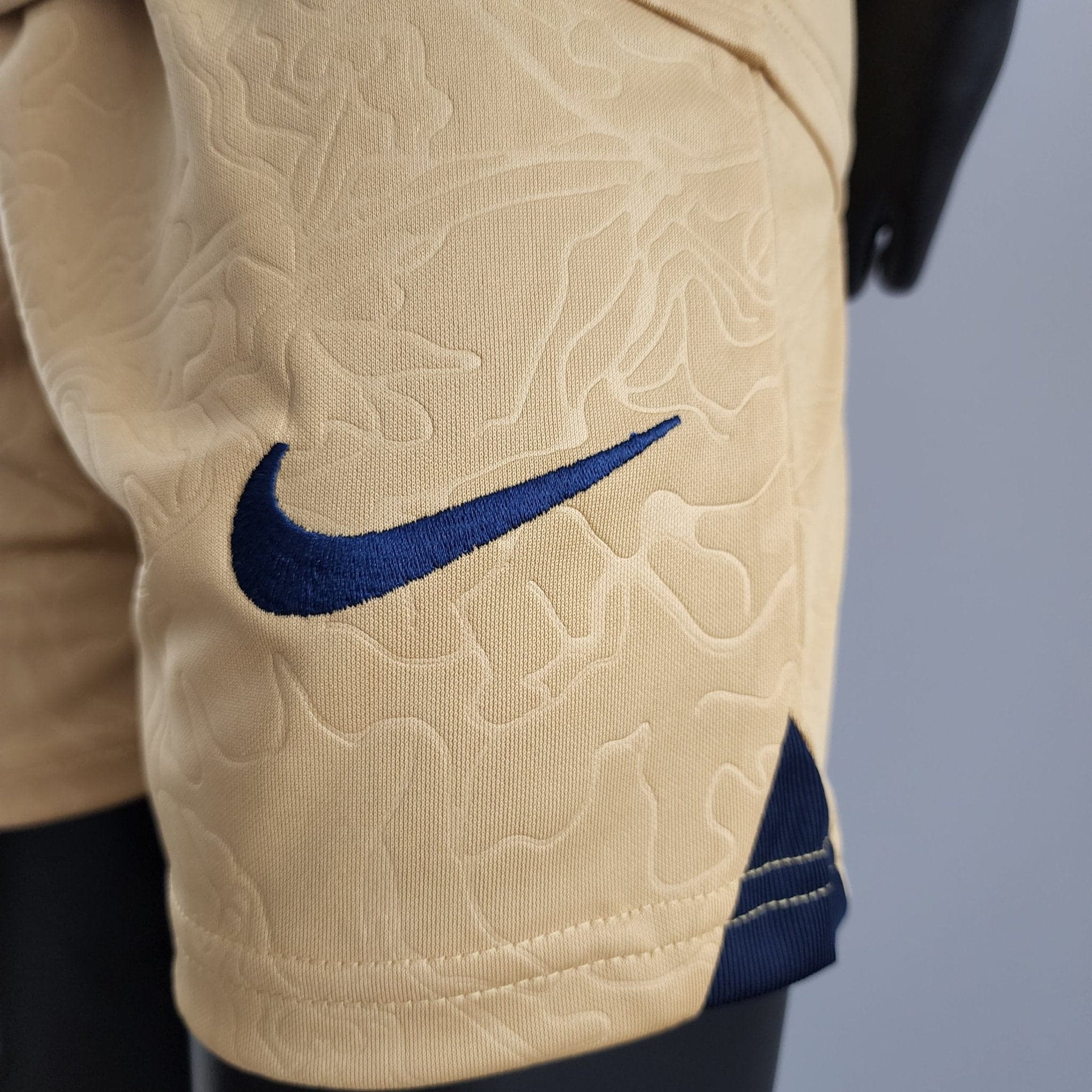 rn-image_picker_lib_temp_79f9f13f-c6c3-47d1-86f4-d1b2e08a77f7 | AE JERSEY Close-up of beige quilted fabric featuring a blue Nike swoosh logo