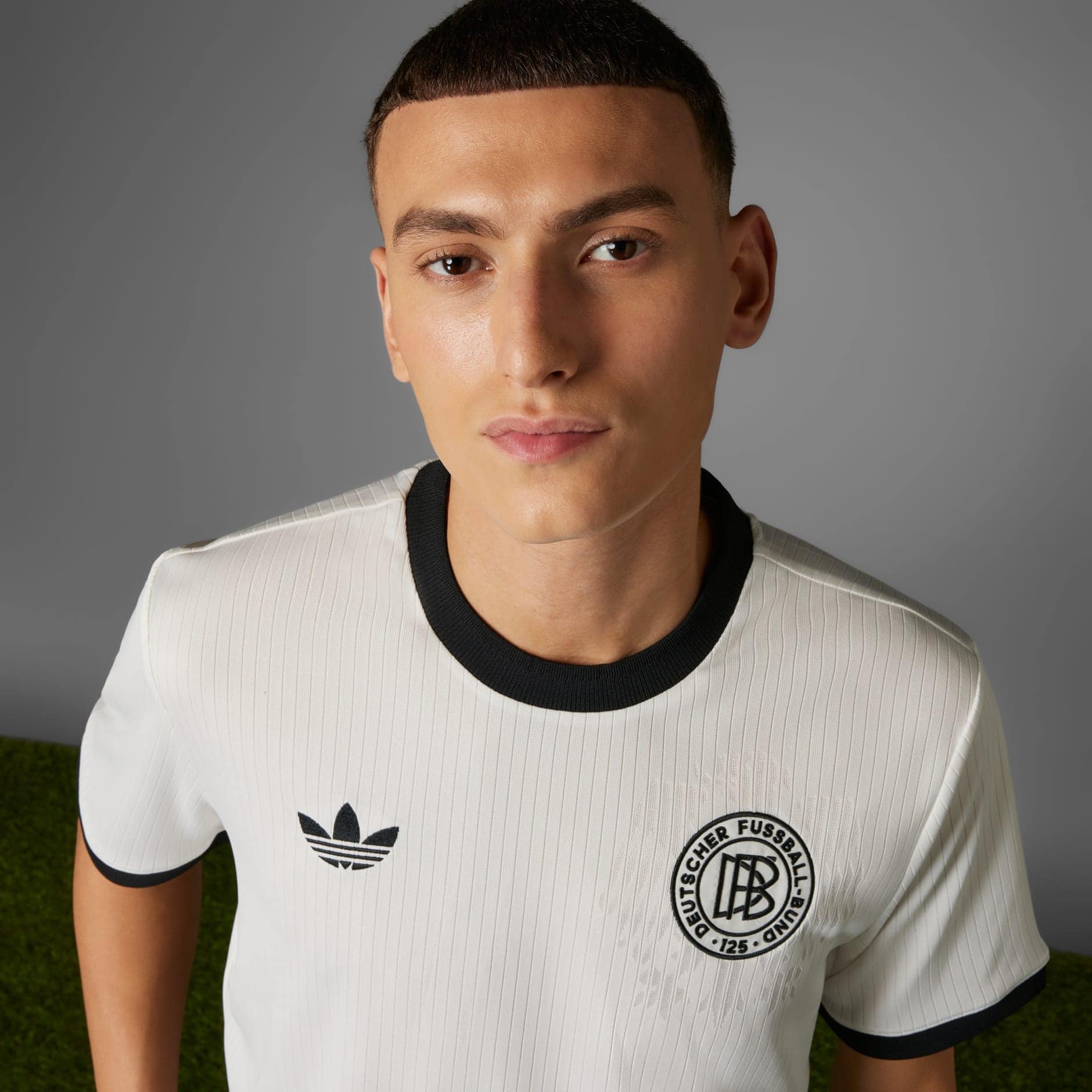 rn-image_picker_lib_temp_a50ebcc3-d44c-4f99-99b9-4bd73e4677a1 | AE JERSEY Close-up of a person wearing a white jersey with black collar, showing Adidas logo and a circular club crest.