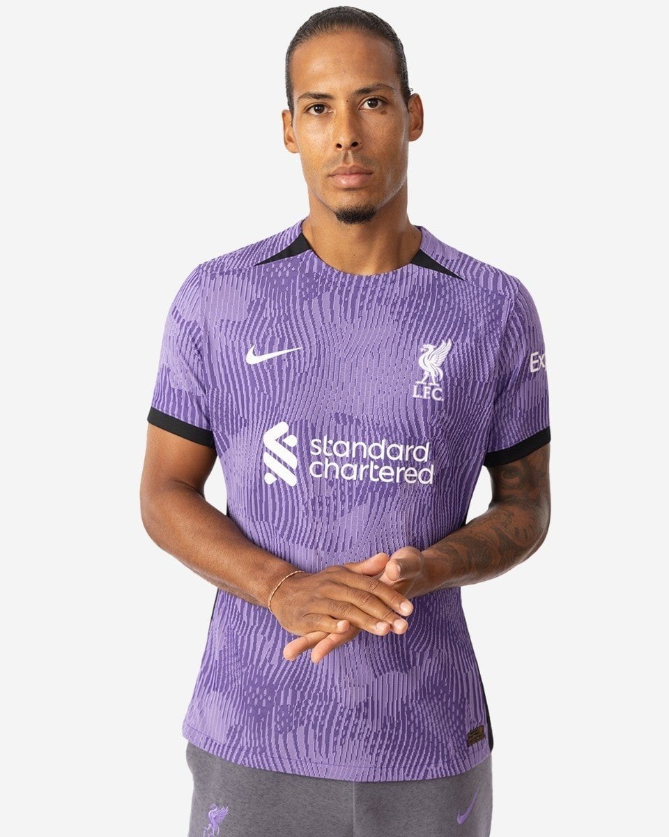 rn-image_picker_lib_temp_bffafafe-9652-4986-afda-9a626368f05c | AE JERSEY Male model wearing a purple Liverpool FC jersey with Standard Chartered sponsor and club crest, standing with hands clasped.