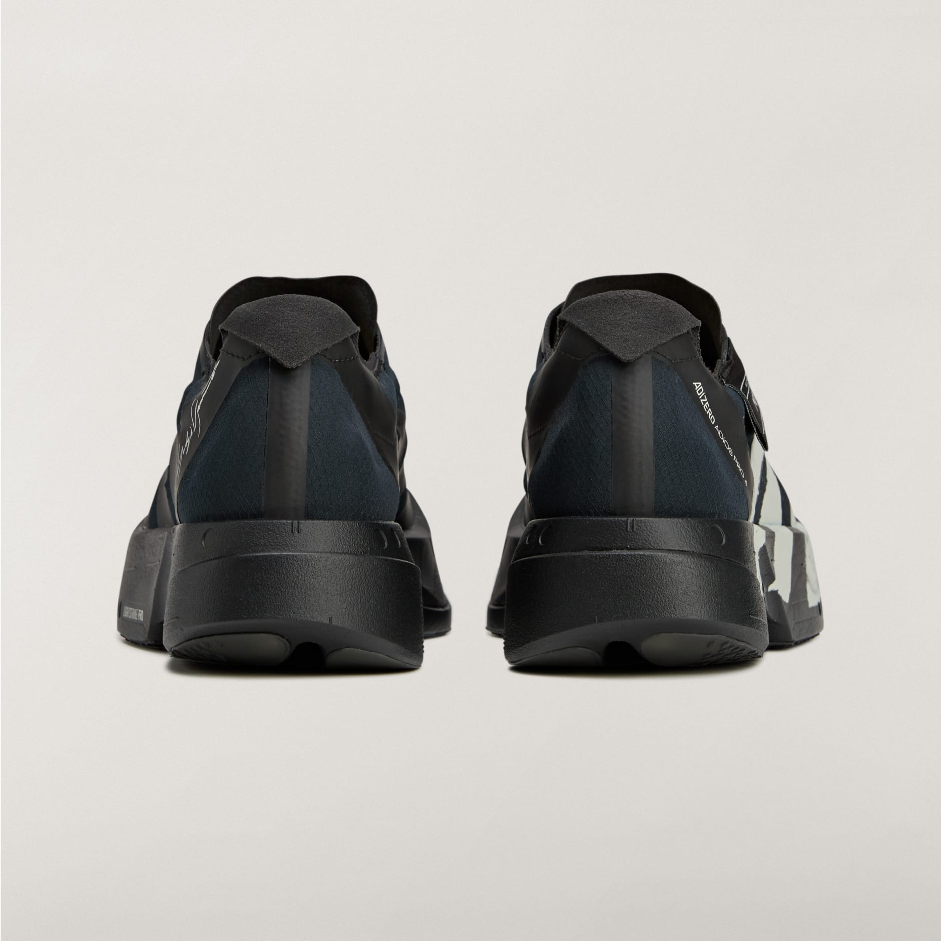rn-image_picker_lib_temp_dfc8a723-521a-4e5b-9f74-ea2ba13f699f | AE JERSEY Rear view of two black athletic sneakers standing side by side on a light background with visible heel straps and soles.