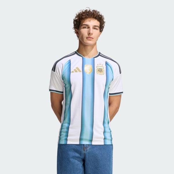 Young man wearing an Argentina national team jersey, standing against a pale gray background.