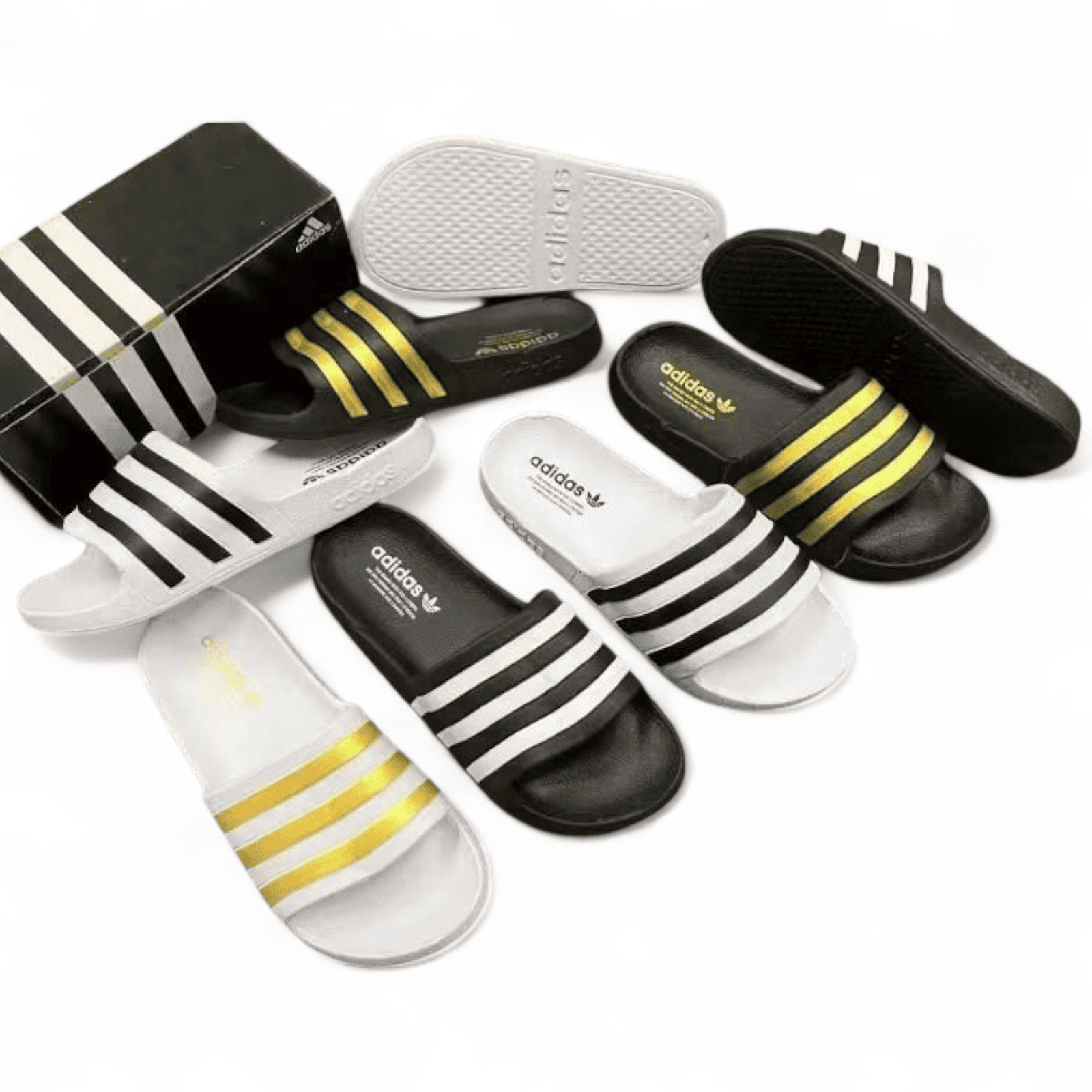rn-image_picker_lib_temp_e0a9af7a-53bb-4dce-9f95-e3dc143591d5 | AE JERSEY Assorted Adidas slide sandals in black and white with yellow stripes, arranged around a black Adidas box.