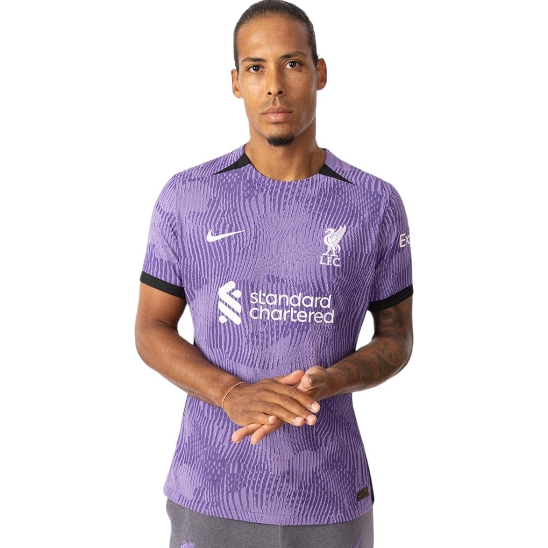 rn-image_picker_lib_temp_eb335c4a-ea34-46ed-bbf3-67d1e630970d | AE JERSEY Man wearing a purple Liverpool FC jersey with Standard Chartered sponsor, facing front with hands clasped.