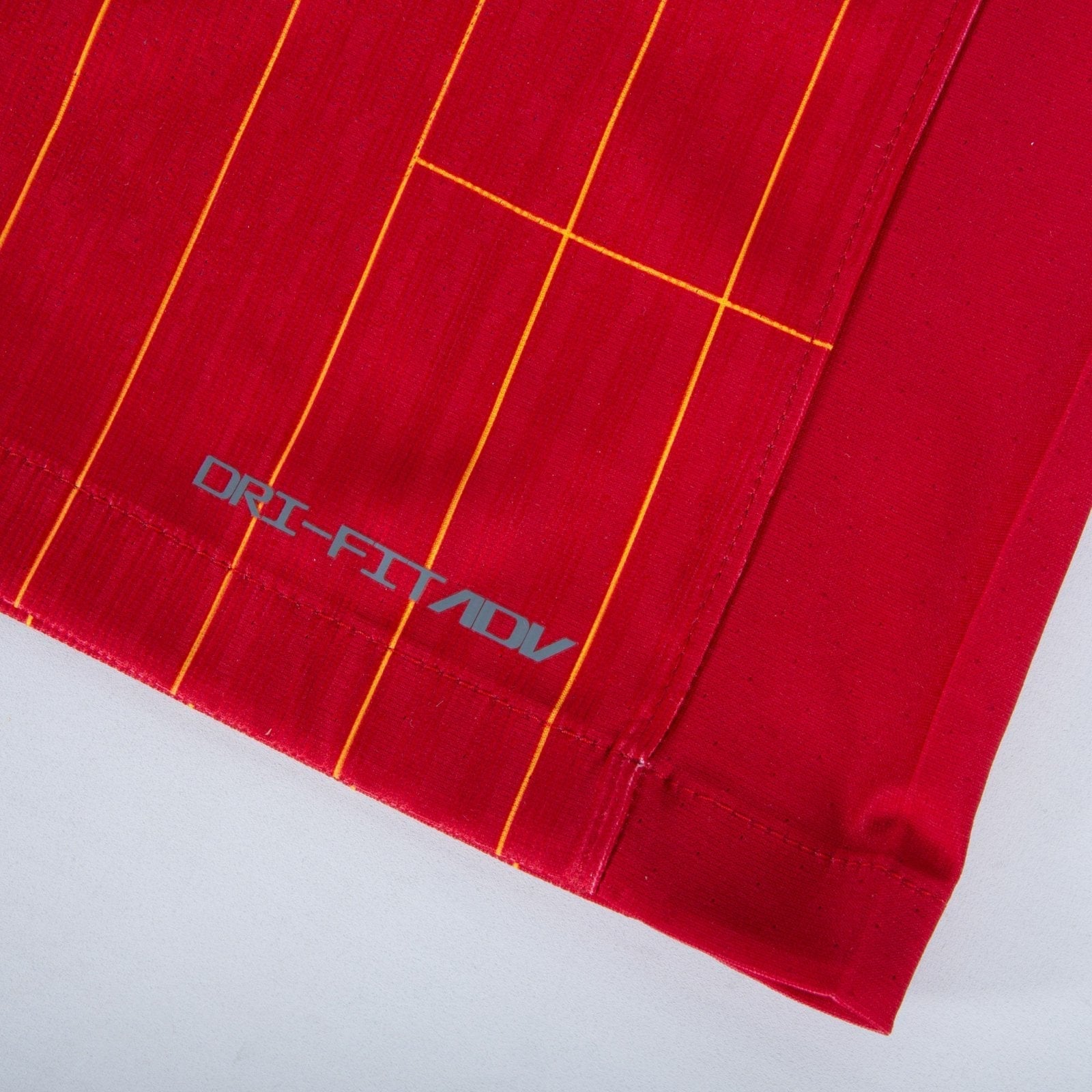rn-image_picker_lib_temp_fa6607fa-0783-4768-a5ba-25d8ea7ce5f0 | AE JERSEY Close-up of red fabric with thin yellow-orange vertical stripes and a partial gray logo reading 'DRIFT' along the edge.