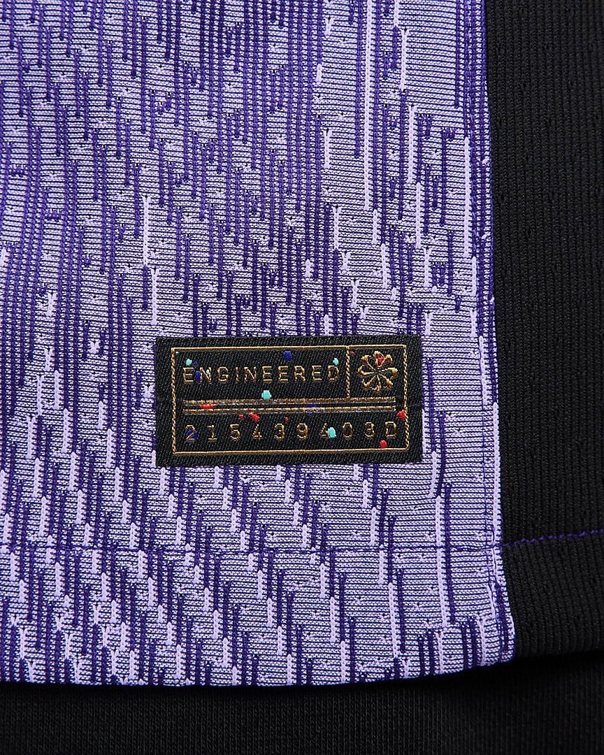 rn-image_picker_lib_temp_fbf162d4-6989-4f18-b32b-e8b98e2b1b23 | AE JERSEY Close-up of purple patterned fabric with a small black tag reading ENGINEERED and a row of numbers nearby.