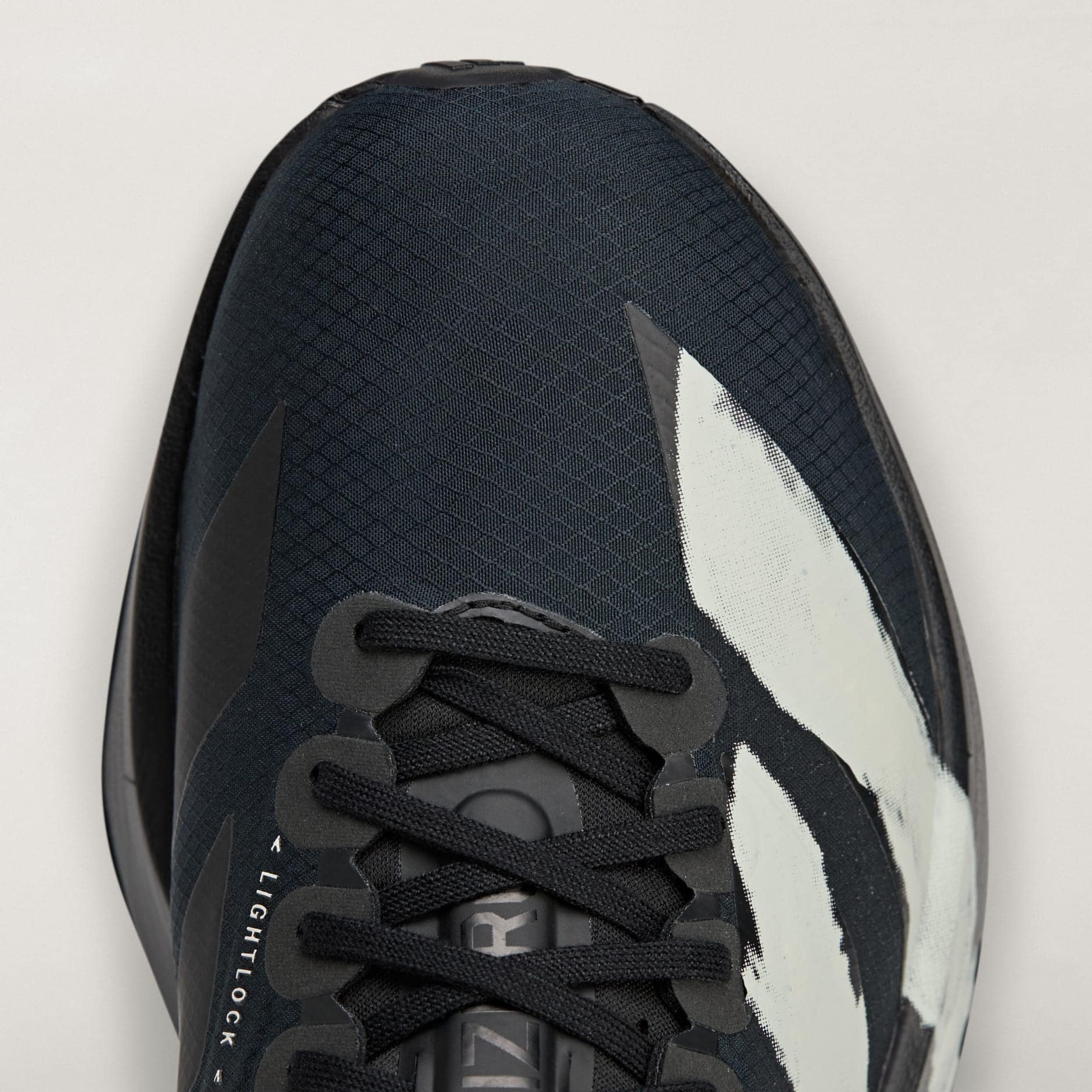 rn-image_picker_lib_temp_fe259813-39c8-4901-935b-93fab09cd81f | AE JERSEY Close-up of a dark athletic sneaker showing laces, textured upper, and a white graphic on a light background