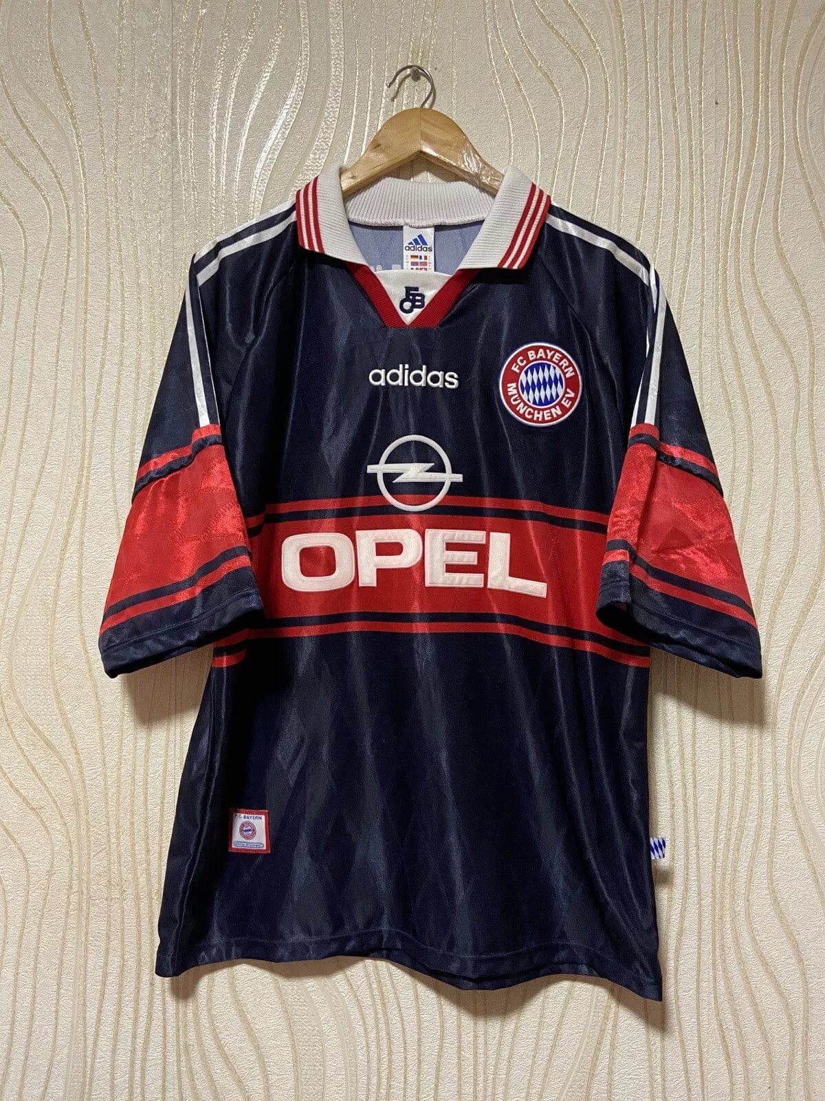 s-l1600_5bc2c7e0-5e29-4dd2-be23-62f0e78b9a2b | AE JERSEY Navy Bayern Munich soccer jersey on hanger with red Opel sponsor and white Adidas logos, FC Bayern badge on chest.