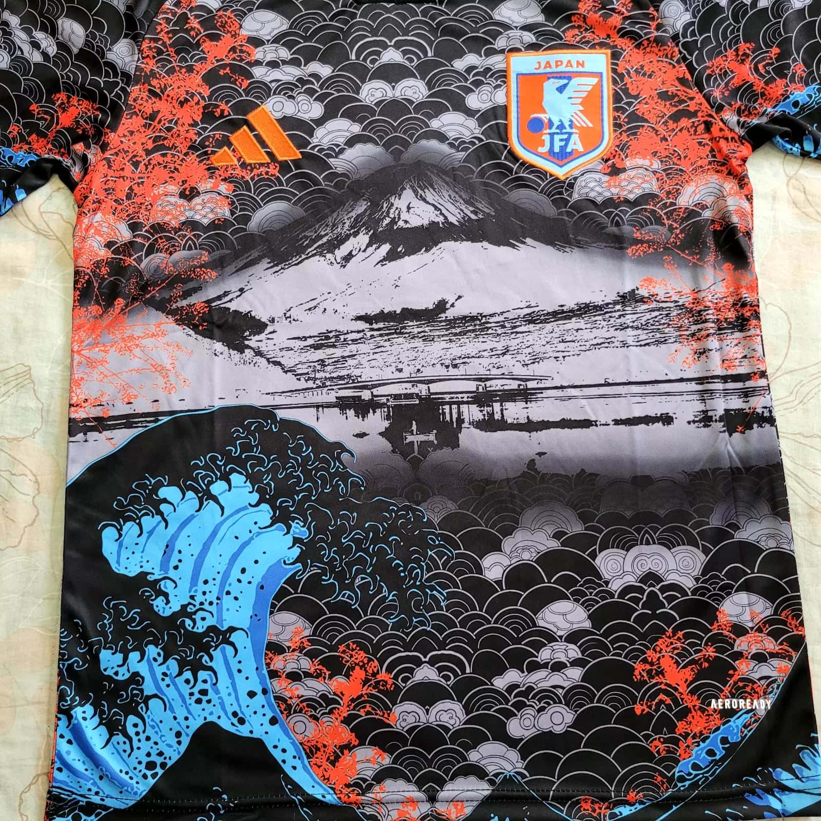 s-l1600_6_c55c5b5d-f3cf-4023-a3fa-5cf63b5369a8 | AE JERSEY Sports jersey featuring black and gray cloud-wave pattern with orange accents, a blue wave motif, and a Japan Football Association crest.