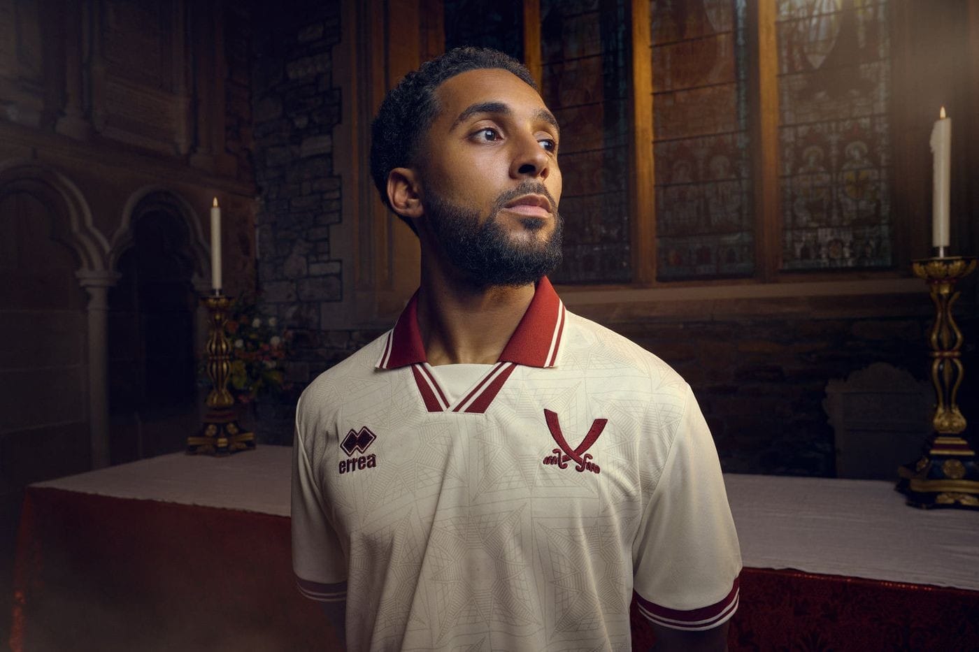 t0tdRPgs9q45zhV | AE JERSEY Portrait of a man in a white maroon-trim soccer jersey, standing by an altar in a church, looking to the side.