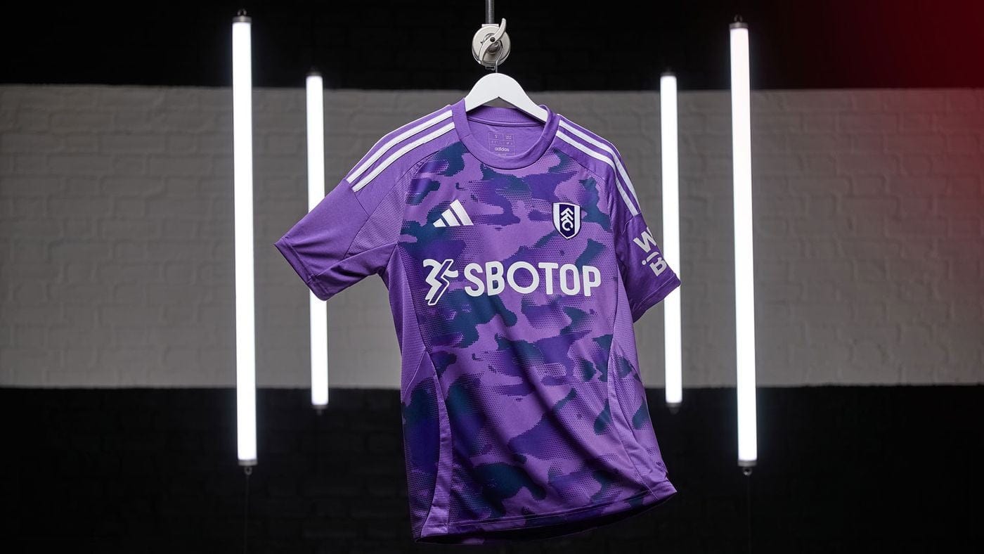 tIXdkIZRUfQmXtW | AE JERSEY Fulham FC purple camouflage soccer jersey with SBOTOP sponsor hanging on a hanger in a studio setting.