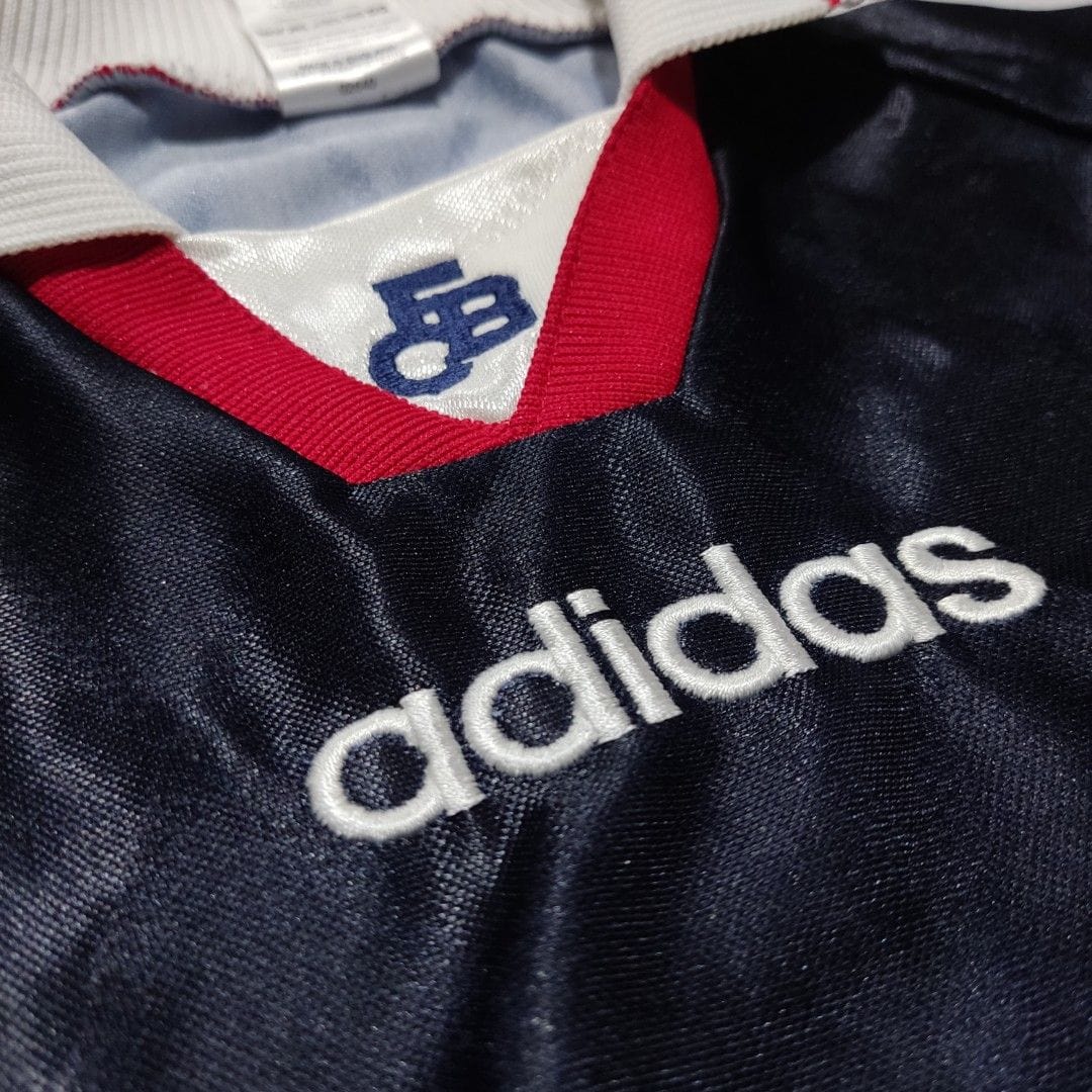vintage_adidas_9799_fc_bayern__1668084639_916d12c5_progressive | AE JERSEY Close-up of a dark navy jersey with white embroidered 'adidas' logo and a red collar detail, fabric sheen visible.
