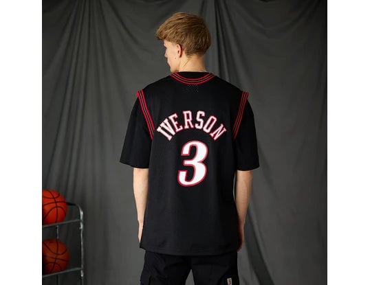 Back view of a person wearing a black basketball jersey with 'IVerson' and the number 3; basketballs on a rack to the left.