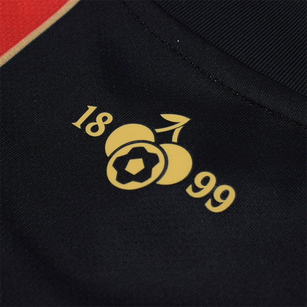 xNUuWCbqjEbBQAR | AE JERSEY Close-up of a black fabric featuring a gold logo with the numbers 18 and 99 and a simple circular fruit motif.
