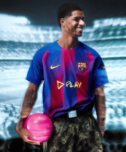 yt | AE JERSEY Smiling male soccer player in FC Barcelona jersey standing in a stadium, holding a pink soccer ball.